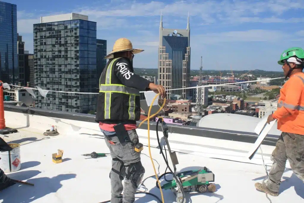 Two Southern Roofing Co roofers heat-welding white TPO membrane seams on a downtown Nashville commercial flat roof